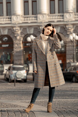 Fototapeta premium Fashionable girl walking down the street in a European city in a stylish coat