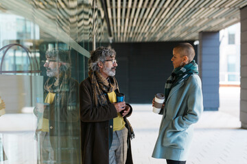 Hispanic colleagues speaking glass wall with takeaway coffee