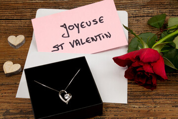 joyeuse saint valentin écrit en Français sur une carte avec un bijou et des rose rouge sur une table
