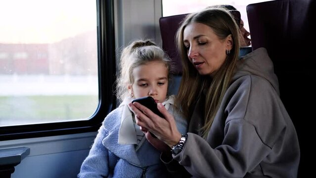 Mom and daughter ride the train and play a game on the phone