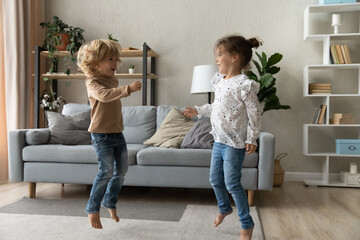 Happy adorable small children siblings dancing to disco pop music on floor carpet in modern living...