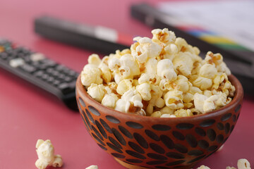 close up of popcorn and Tv remote on red background 