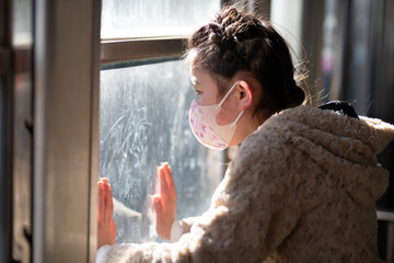 マスクをして窓の外を見る少女