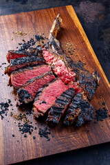 Modern style barbecue dry aged chianina tomahawk steak sliced and served as close-up on a wooden...