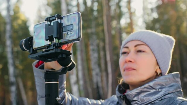 Woman Holding On Handheld Film 3-axis Gimbal Stabilization Device in Winter for Smartphone. Girl Blogger Make Selfie, Broadcast Video Blogging, Vlogging. Videographer Operator Take Photo Video.