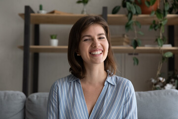 Head shot happy beautiful young 30s woman looking at camera, sitting on sofa. holding video call conversation at home. Joyful female blogger recording video, streaming online showing perfect smile.