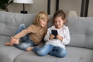 Joyful small kid girl holding cellphone in hands, using modern tech gadget with smiling cute little...