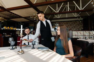 A stylish waiter serves a young couple of a man and a woman who came on a date to a gourmet restaurant. Customer service in the restaurant and catering establishments.