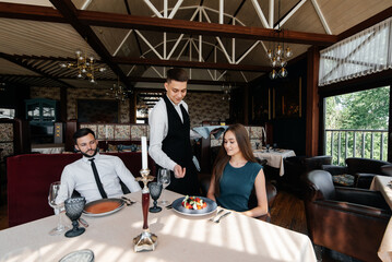 A stylish waiter serves a young couple of a man and a woman who came on a date to a gourmet restaurant. Customer service in the restaurant and catering establishments.