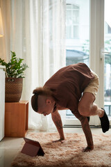Strong young man watching tutorial on tablet computer when learning how to do handstand