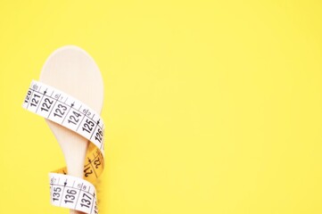 concetto di dieta - metro a nastro avvolto su di un cucchiaio in legno su sfondo giallo con spazio...