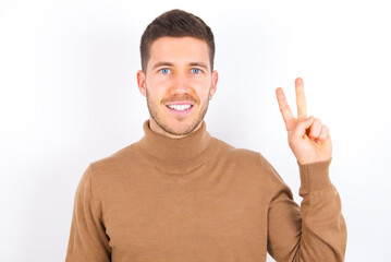 young caucasian man wearing grey turtleneck over white background showing and pointing up with fingers number two while smiling confident and happy.