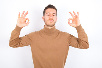 young caucasian man wearing grey turtleneck over white background relax and smiling with eyes closed doing meditation gesture with fingers. Yoga concept.