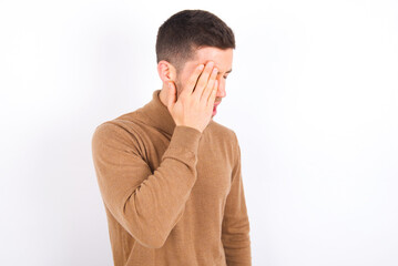 Fototapeta premium young caucasian man wearing grey turtleneck over white background Yawning tired covering half face, eye and mouth with hand. Face hurts in pain.