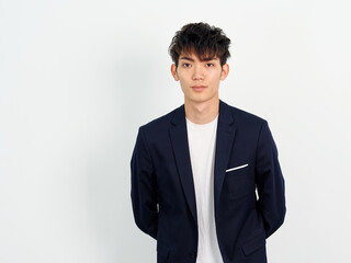 Portrait of handsome Chinese young man in dark blue leisure suit posing against white wall background. Arms on back and looking at camera, looks confident, front view.