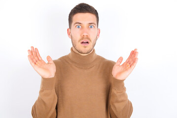 Surprised terrified young caucasian man wearing grey turtleneck Gestures with uncertainty, stares...
