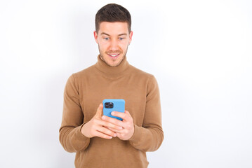 young caucasian man wearing grey turtleneck over white background using mobile phone chatting free time .