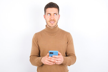 young caucasian man wearing grey turtleneck over white background hold telephone hands read good youth news look empty space advert
