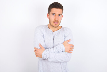 young caucasian man wearing grey sweater over white background shaking and freezing for winter cold with sad and shock expression on face.