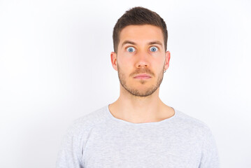Stunned young caucasian man wearing grey sweater over white background stares reacts on shocking...