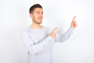 young caucasian man wearing grey sweater over white background smile excited directing fingers look empty space