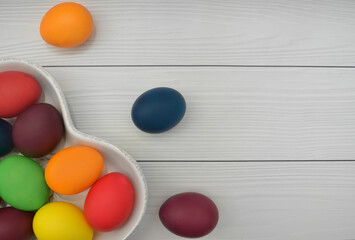 Easter concept: green, orange, yellow, pink, red, purple and blue dyed or painted eggs in a white plate in the shape of a heart on a white background. Flat lay, top view.