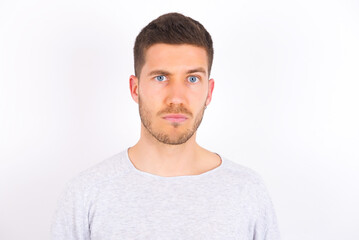 Fototapeta premium Displeased young caucasian man wearing grey sweater over white background frowns face feels unhappy has some problems. Negative emotions and feelings concept