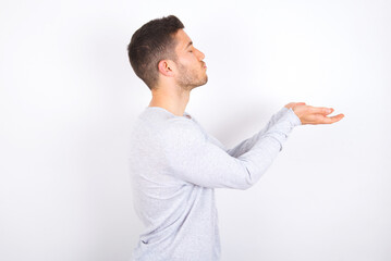 Profile side view view portrait of attractive young caucasian man wearing grey sweater over white background sending air kiss