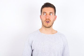 Obraz premium Shocked young caucasian man wearing grey sweater over white background look empty space with open mouth screaming: Oh My God! I can't believe this.