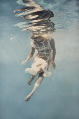 A woman in a dress swims underwater as if floating in zero gravity