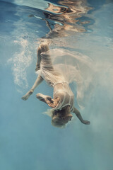 A woman in a dress swims underwater as if floating in zero gravity