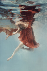 A woman in a dress swims underwater as if floating in zero gravity