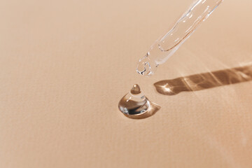 Transparent drop of hyaluronic acid on an orange background with a glass pipette, body moisturizer close-up, top view.