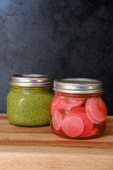 Jar of pesto and pickled radishes in front of a rustic background