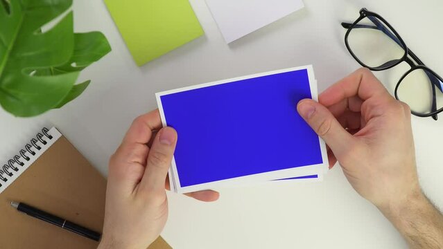 take two paper card. Top view male hands Photo on white background. Blue chroma key image. Place for text or your photos. Desktop in the office. Glasses and notebook top view. Take paper and clean up