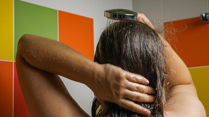 A woman sprays dry, long, dark hair from the shower. There are colorful tiles in the background....