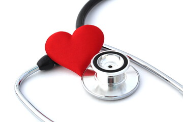 On a white isolated background lies a black stethoscope and a red heart lies nearby.