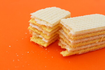 Two slices of broken one waffle lies on an orange background.