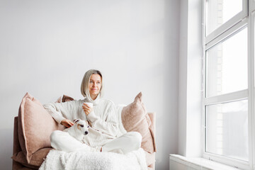 Relaxed, serene adult woman drinking cup of coffee on the sofa in the living room