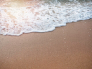 Fototapeta na wymiar Blurred white splashing sea wave on sand beach with copy space. Blurry summer sunset beach background.