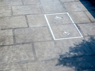 The old white handicapped icon symbol on the ground shows a sign reserved for disabled persons in a car parking space, top view.