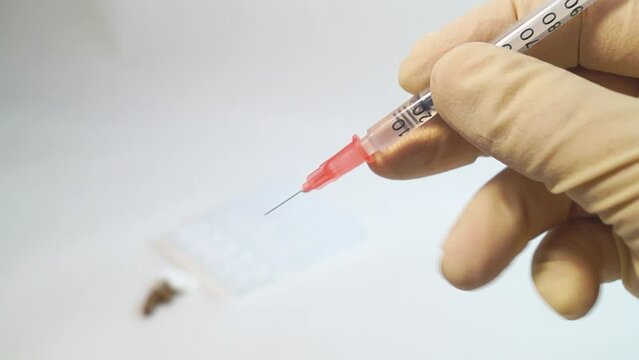 The cap is removed from the insulin syringe with hands in medical gloves
