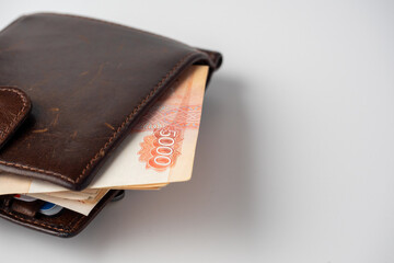 A close-up of a leather wallet full of 5000 rubles banknotes lies on a white background. Side view, copy space