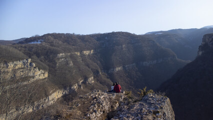 Couple in love sits on a cliff in the mountains winter landscape