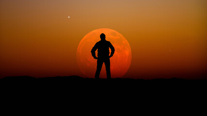 Man observing evening sky with stars, planets and full Moon rising behind the horizon.