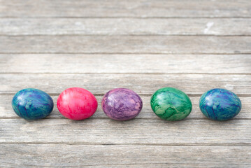 Several brightly painted eggs lie side by side on a wooden background at Easter, with space for text