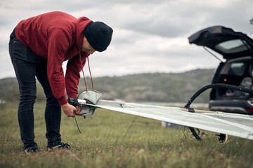 Windsurfer unpacking equipment from a car in nature near the lake shore.