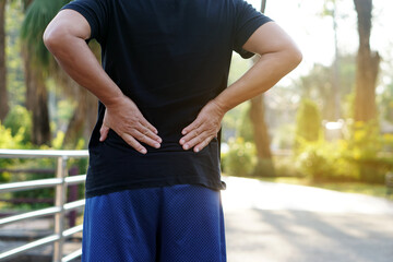 Man hurt his waist or back after running and exercise outdoor in the park. Use hands to touch his...