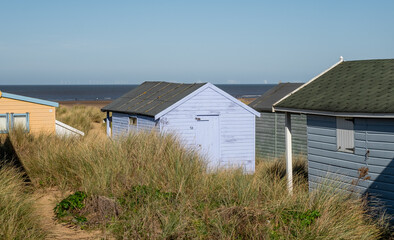 Fototapeta na wymiar Traditional wooden beach hut in the sand dunes on a bright and sunny day on Hunstanton beach, North Norfolk coast.