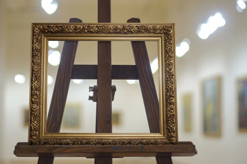 An empty golden frame on the wooden easel with blurred gallery background, selective focus